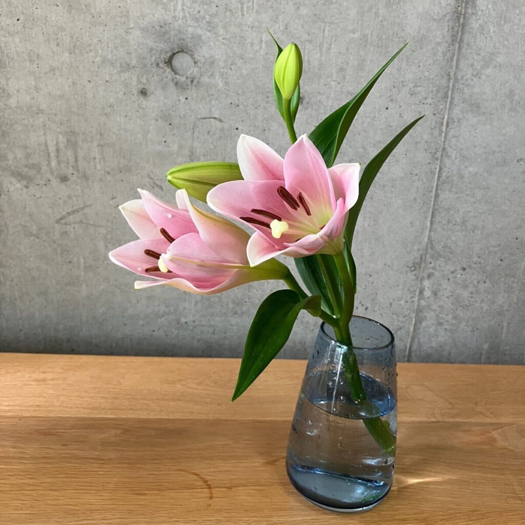 medeluのANYROOMコースのボリュームBasicのテッポウユリを青の透明ガラス花瓶に生けた様子