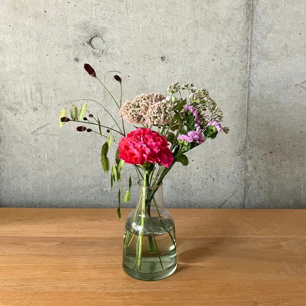 POSH LIVING ガラスボトル グリーンに花の定期便medeluから届いたカーネーション、スターチスなどを生けた様子