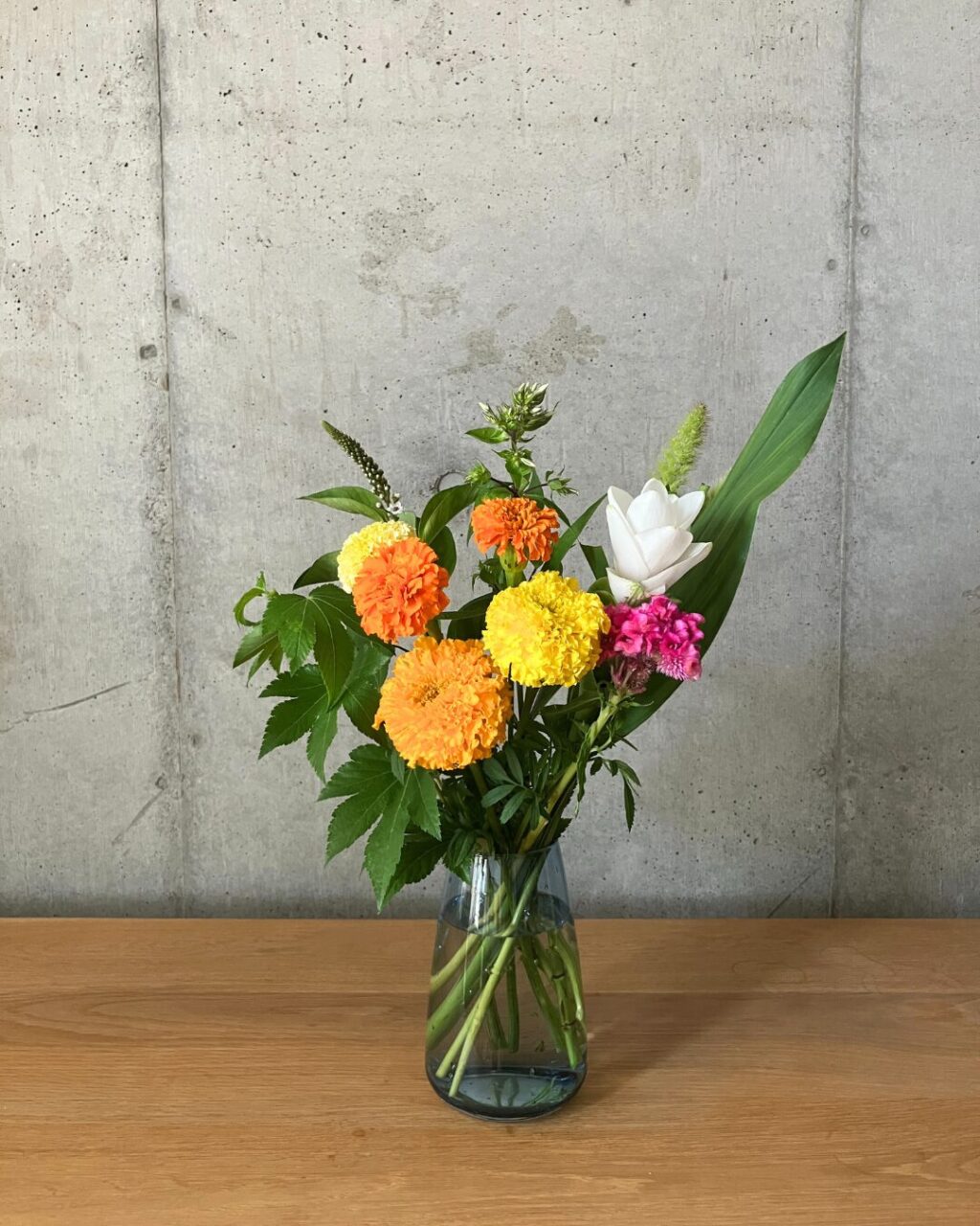 マリーゴールドなどのイエロー＆オレンジ系のお花をブルーの色付きの花瓶に生けた様子