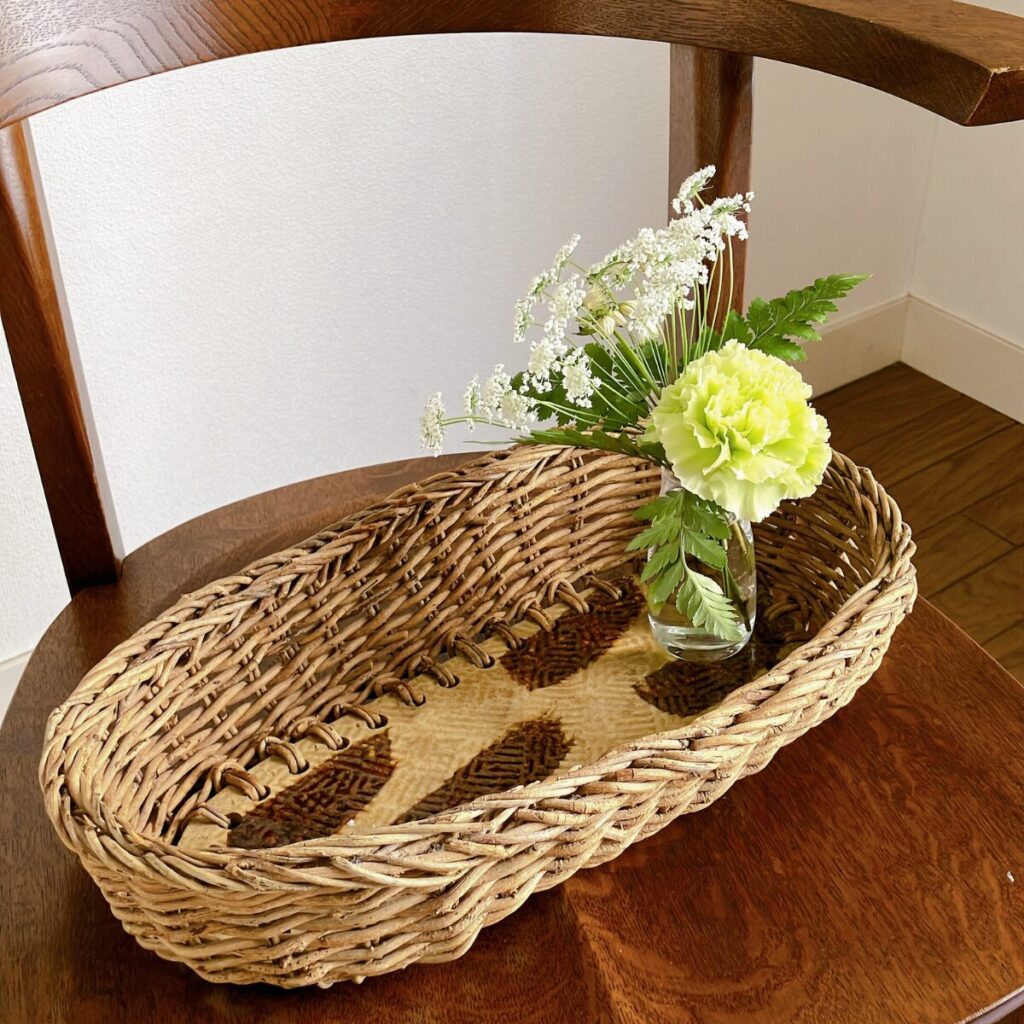 底がタイルのカゴにカーネーションやレースフラワーなど数本のお花を花瓶ごと飾っている様子