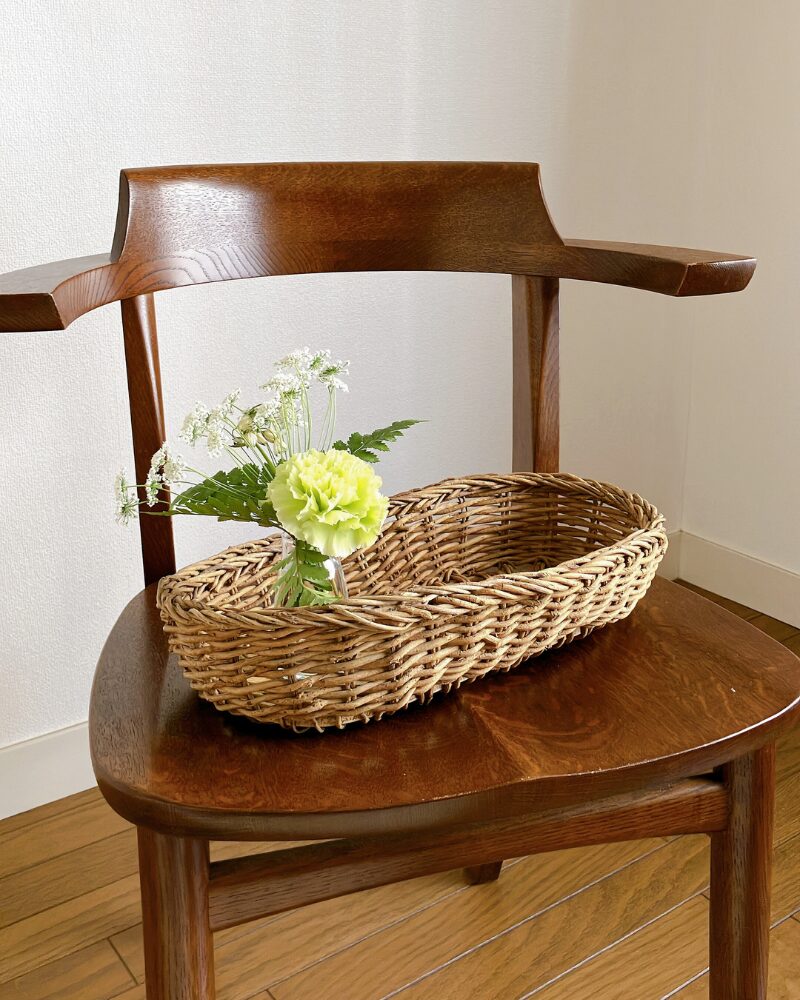 カーネーションとレースフラワーを小さな花瓶に生けて底がタイルになっているカゴに飾った様子の引きの写真