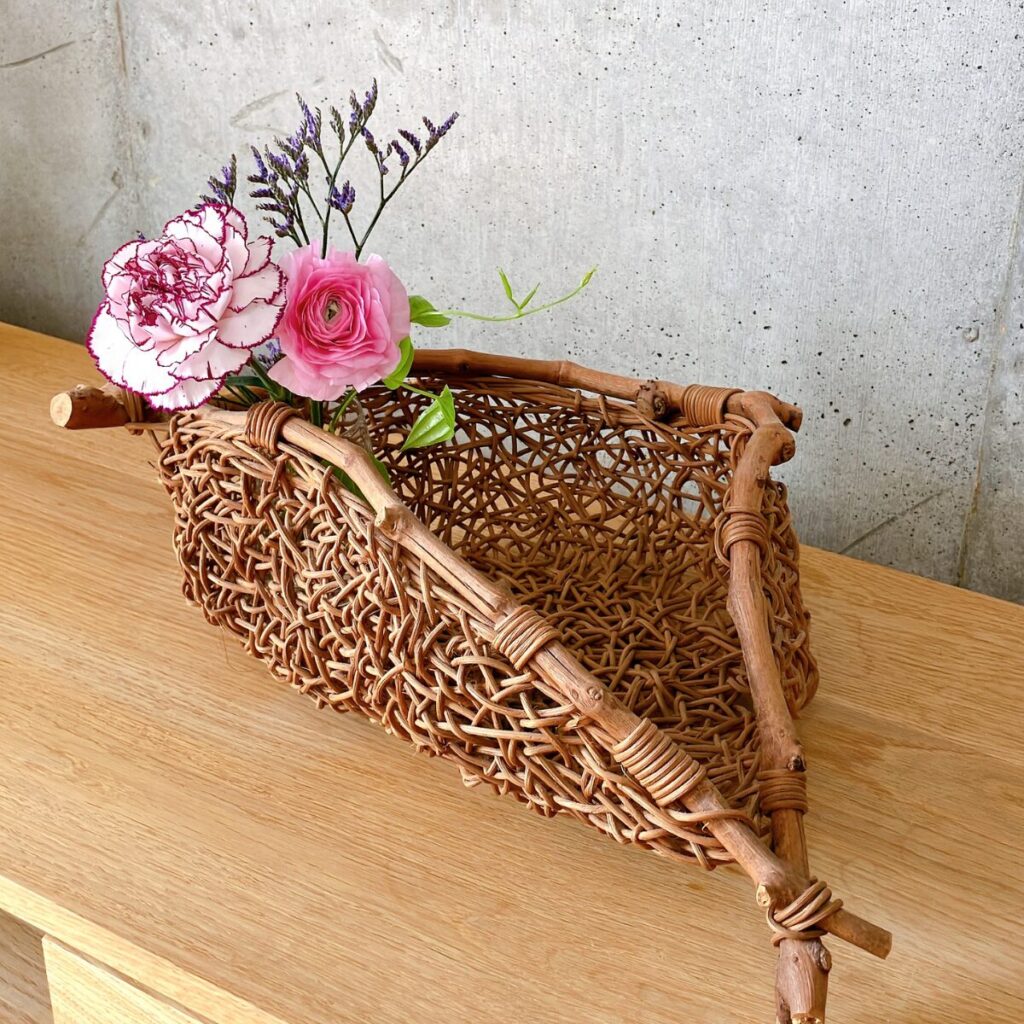 フルーツバスケットにバラやラナンキュラスなど数本のお花を花瓶ごと飾っている様子