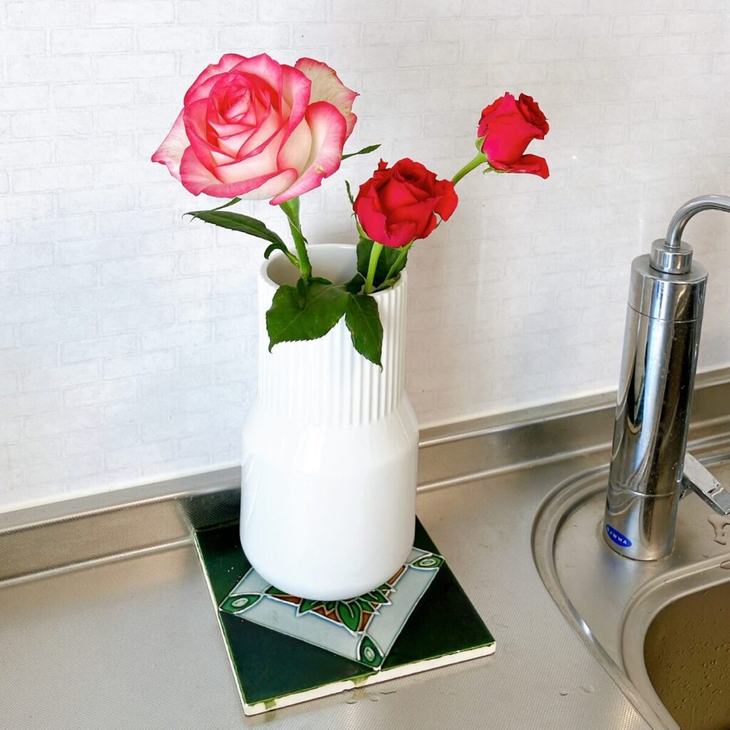 3本のバラを陶器の花瓶に生けて、タイルの上に飾っている様子