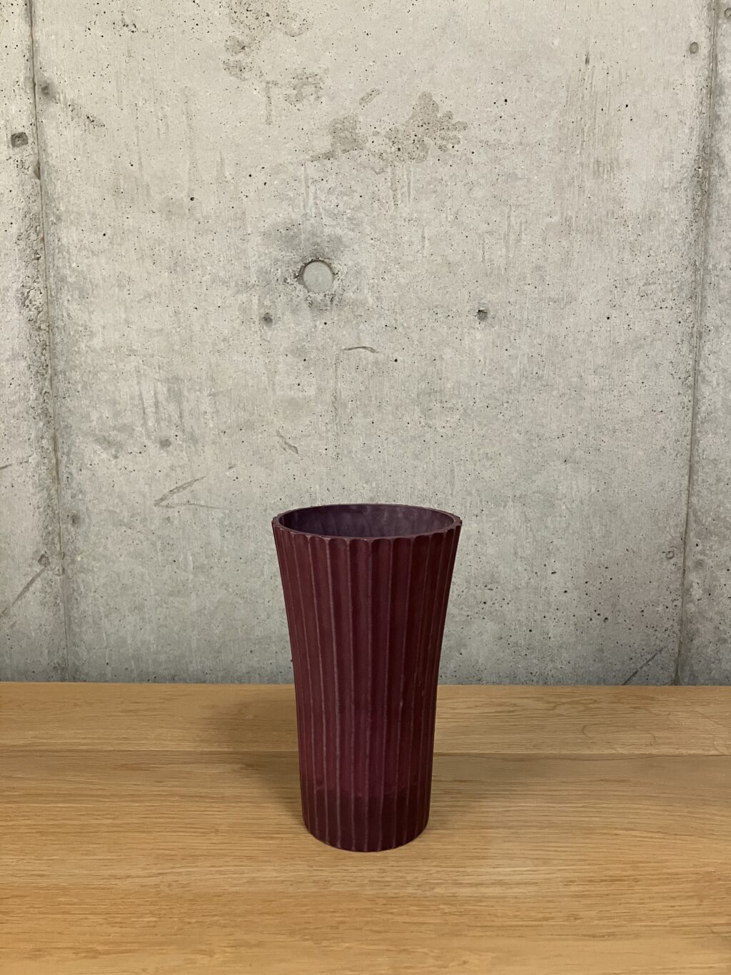 フラワーアレンジメントに使用している濃い色の樹脂製花器。少し高さのあるシュッとした形状。