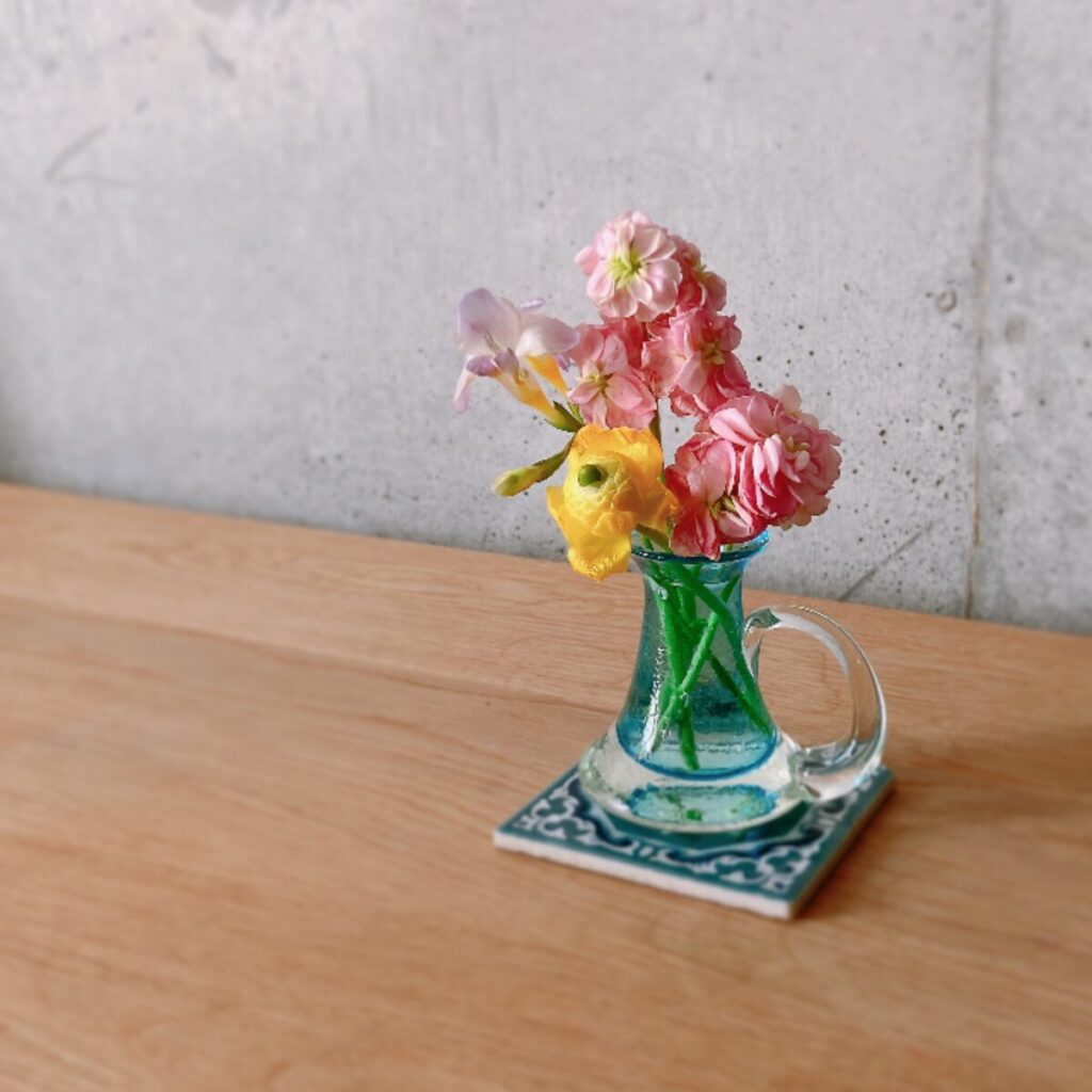 タイルの上に小さいお花を集めて生けているガラスのミルクピッチャーを置いている様子