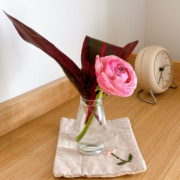 ラナンキュラスとドナセラを生けたガラス花瓶をコースターの上に置いている様子