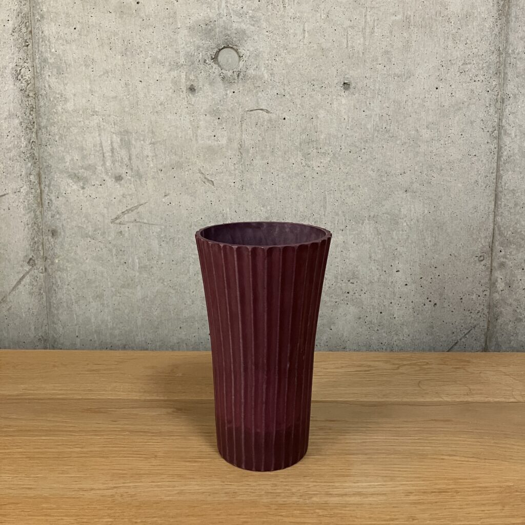 フラワーアレンジメントに使用している濃い色の樹脂製花器。少し高さのあるシュッとした形状。
