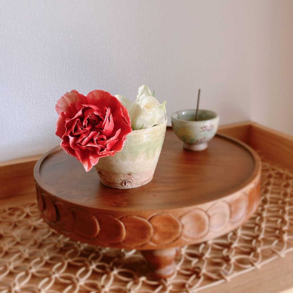 Red-orange and white carnations in a teacup on a rattan mat with incense