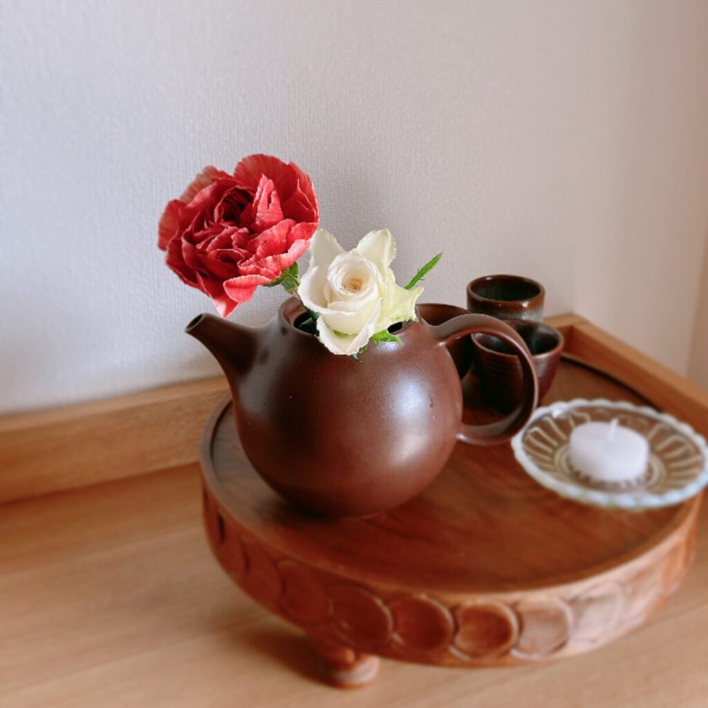 Carnations in a brown teapot with three matching sake cups and a candle.