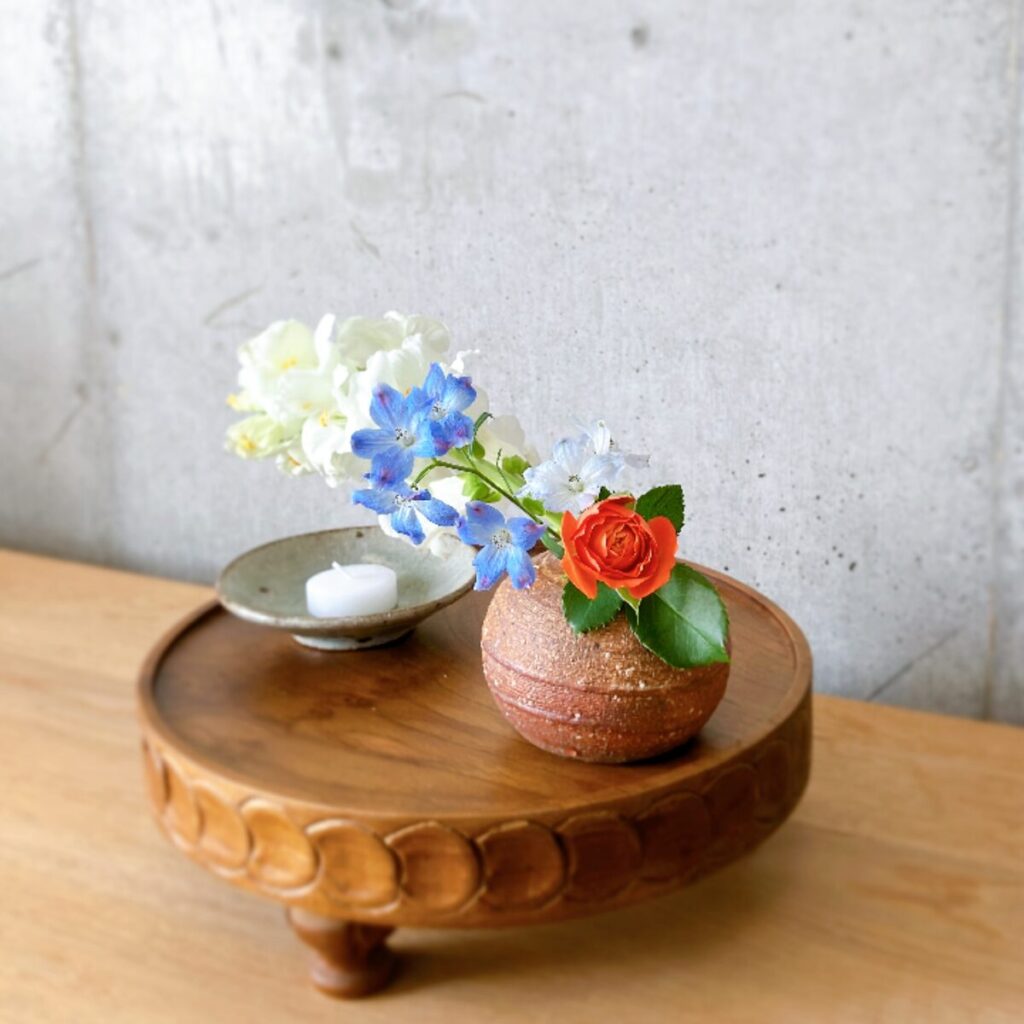 Kasama-yaki round vase with orange roses and delphiniums next to a low candle