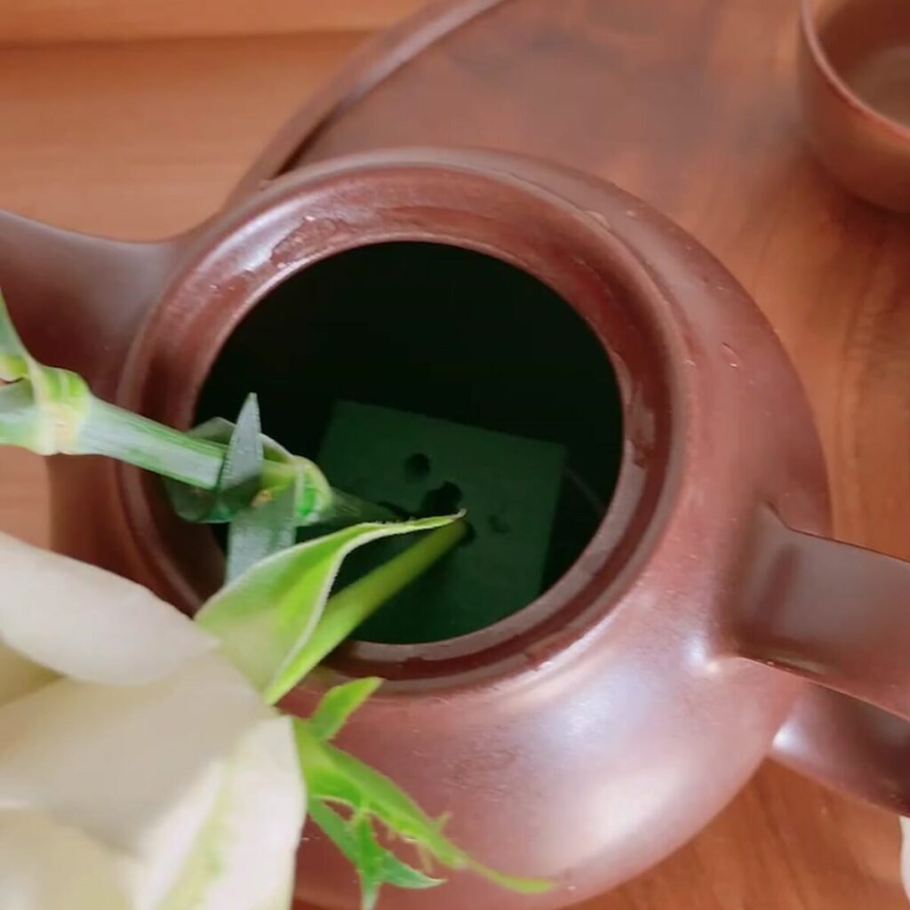 Close-up of carnations in a traditional Japanese brown teapot, with the green floral foam (Oasis) used for stabilization clearly visible inside