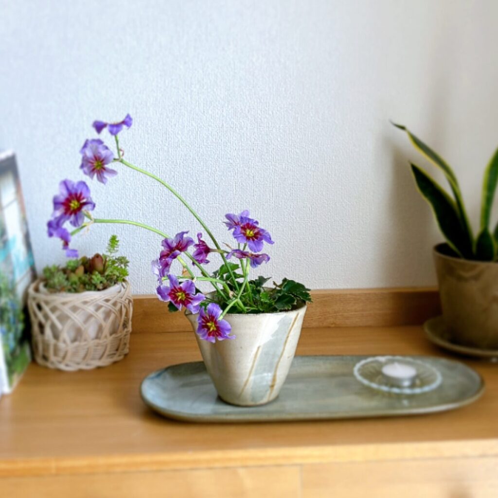 Finished Leucocoryne arrangement in a pitcher, styled on a long plate with a low candle