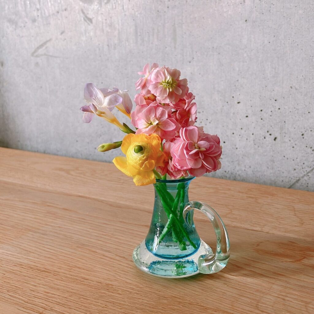 小さい短いストックやラナンキュラス、フリージアを集めてミルクピッチャーに生けた様子