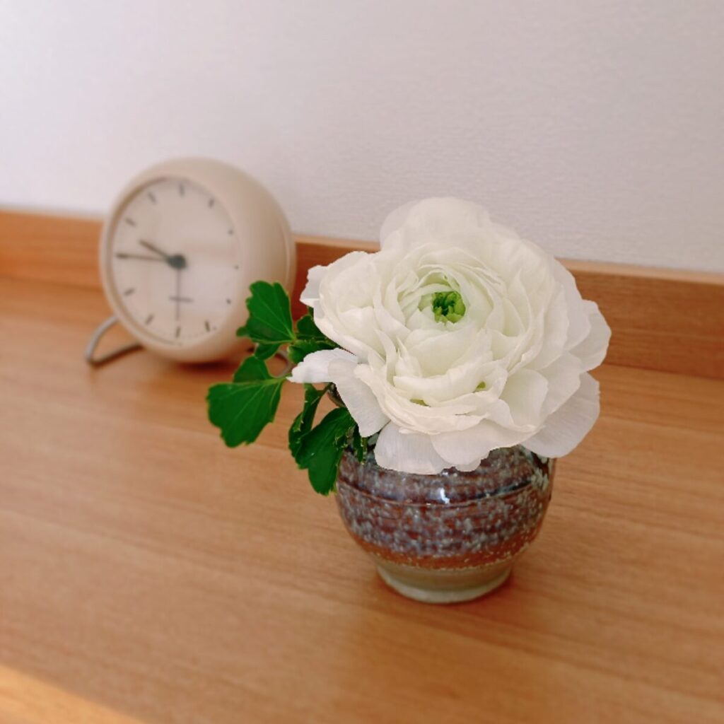 丸い和の陶器花瓶に白いラナンキュラスとグリーンを添えた様子