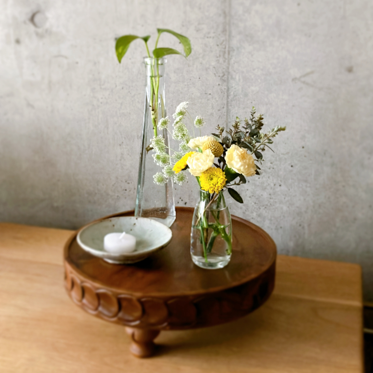 木のコンポートにろうそく、ポトス、小さなお花のブーケを置いた様子