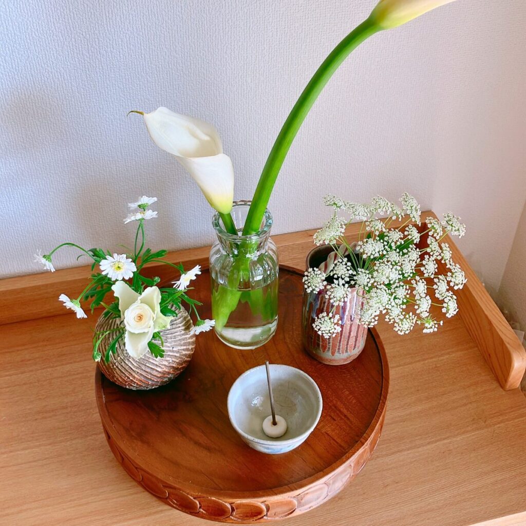 Close-up of tall calla lilies and white flowers in mixed ceramic and clear glass vases on a wooden surface
