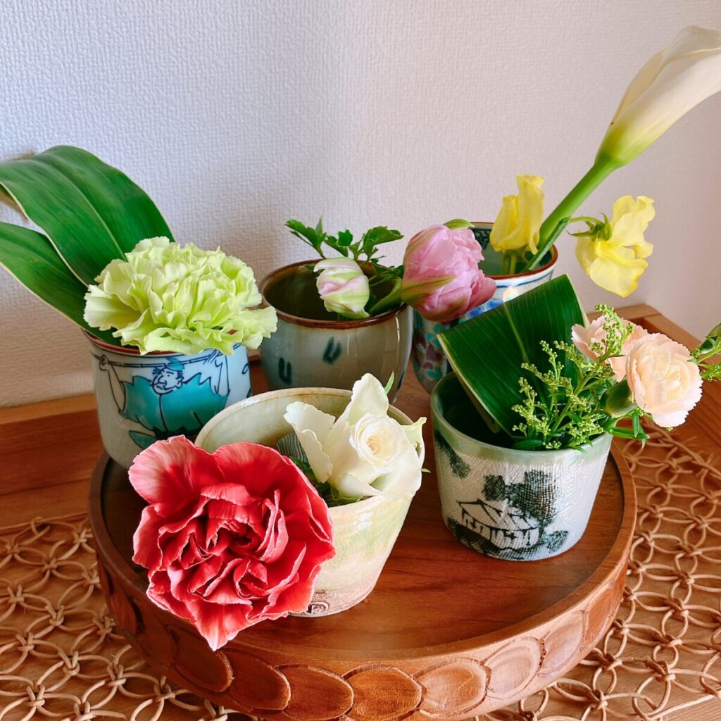 Detailed close-up of small colorful flower arrangements in distinct Japanese tea cups and soba-choko