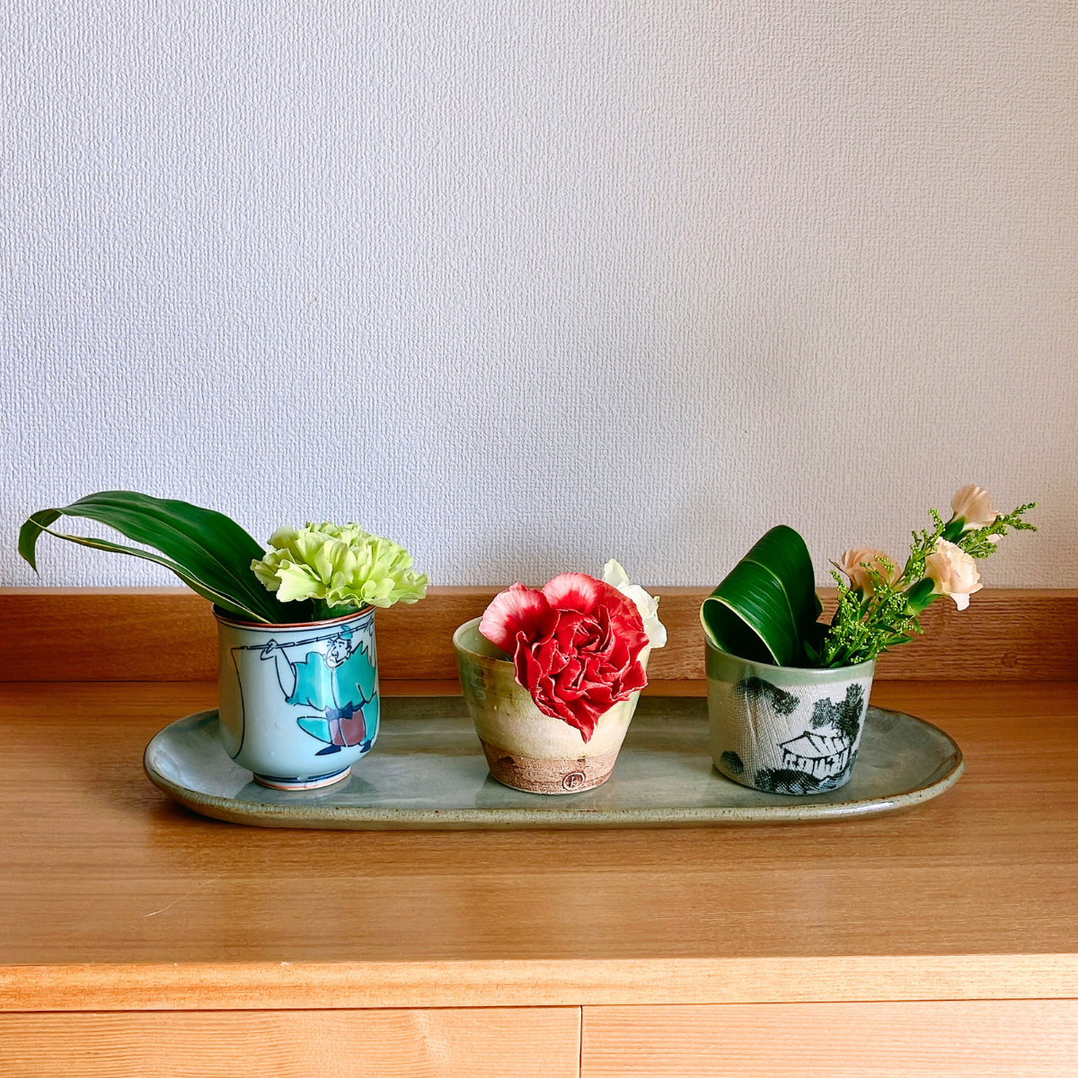 湯呑み・蕎麦猪口など、3つのお花を生けた器をお皿に並べた様子