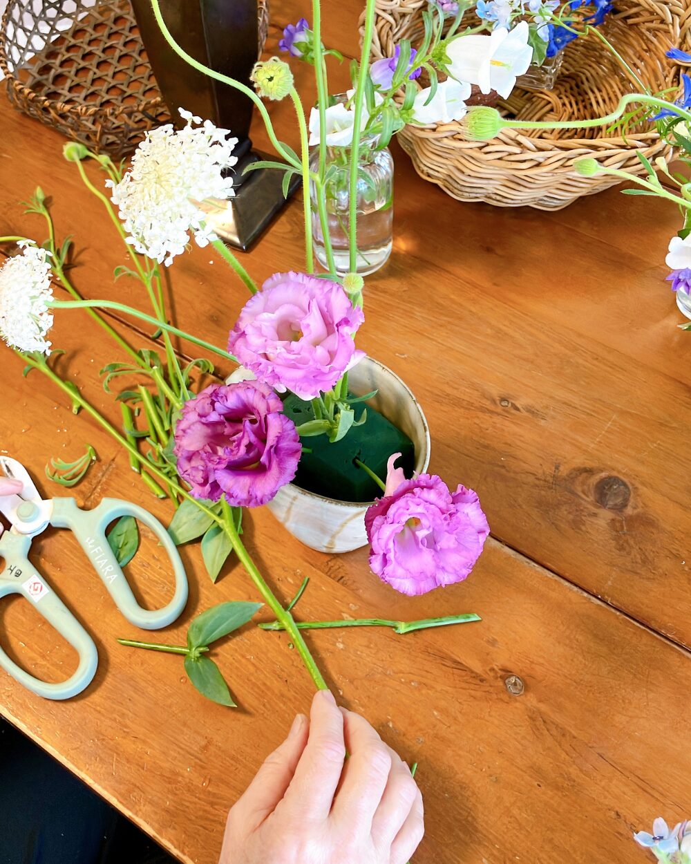 Arranging purple Lisianthus in a ceramic pitcher using floral foam for steady placement