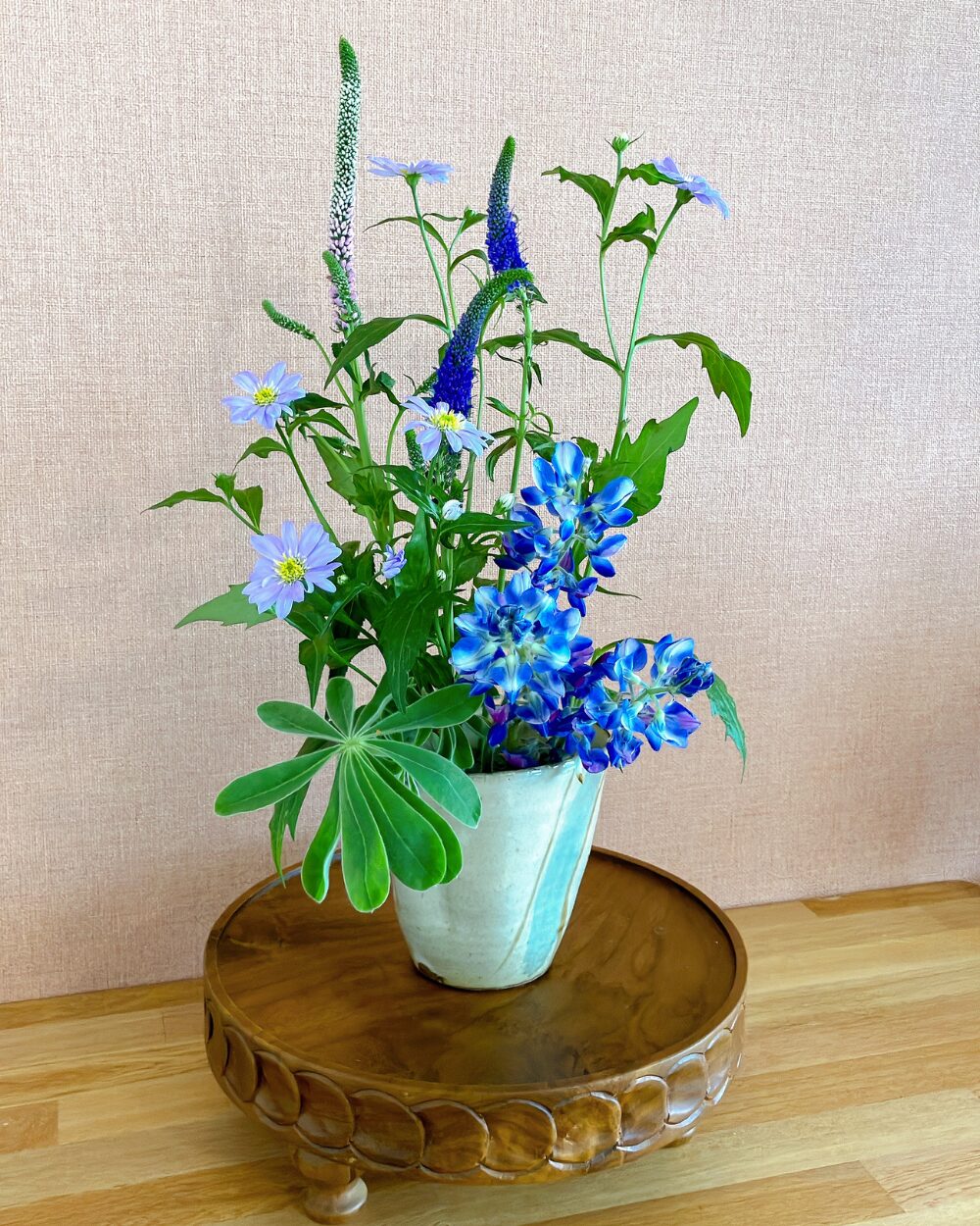 A rustic and dense flower arrangement with blue lupinus and purple blossoms in a ceramic vessel
