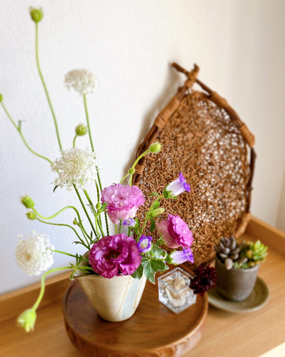 Close-up of purple Lisianthus and curved white flowers on a dark wooden compote