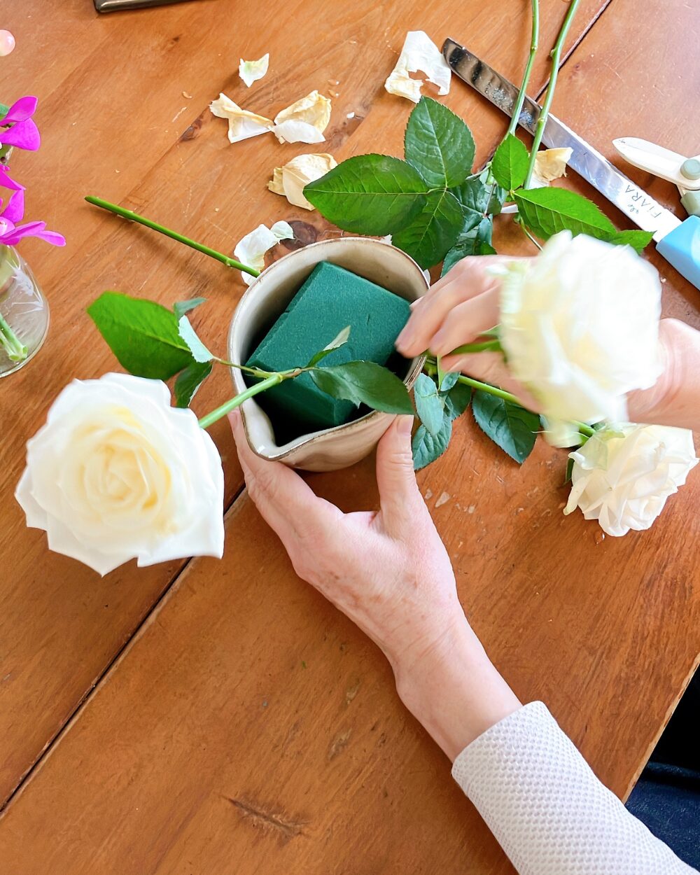 Close-up of a person's hand inserting white roses into floral foam for styling