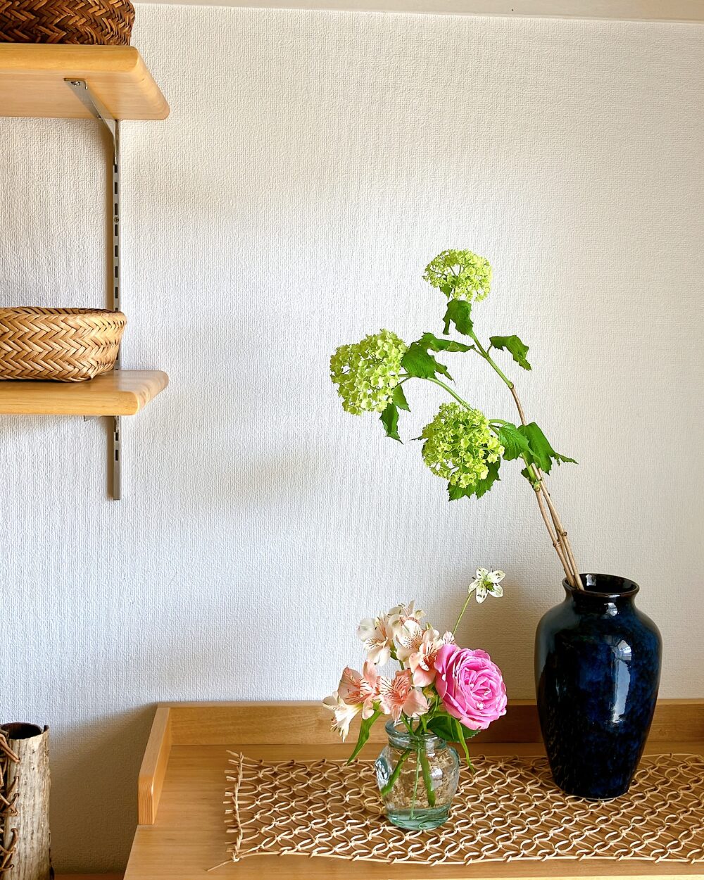 A two-tier floral arrangement in a Japandi-style interior featuring traditional pottery and early summer flowers