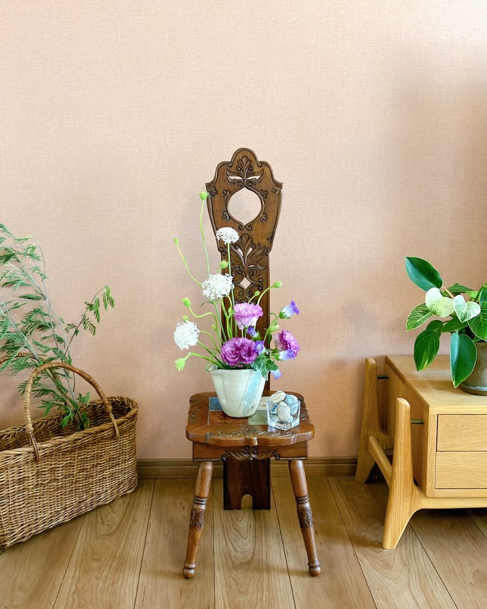 Purple flower arrangement on a wooden chair against a warm orange wall