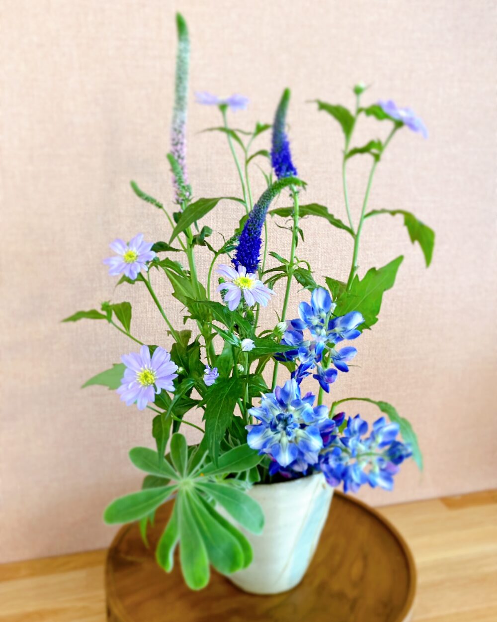 A rustic and dense flower arrangement with blue lupinus and purple blossoms in a ceramic vessel