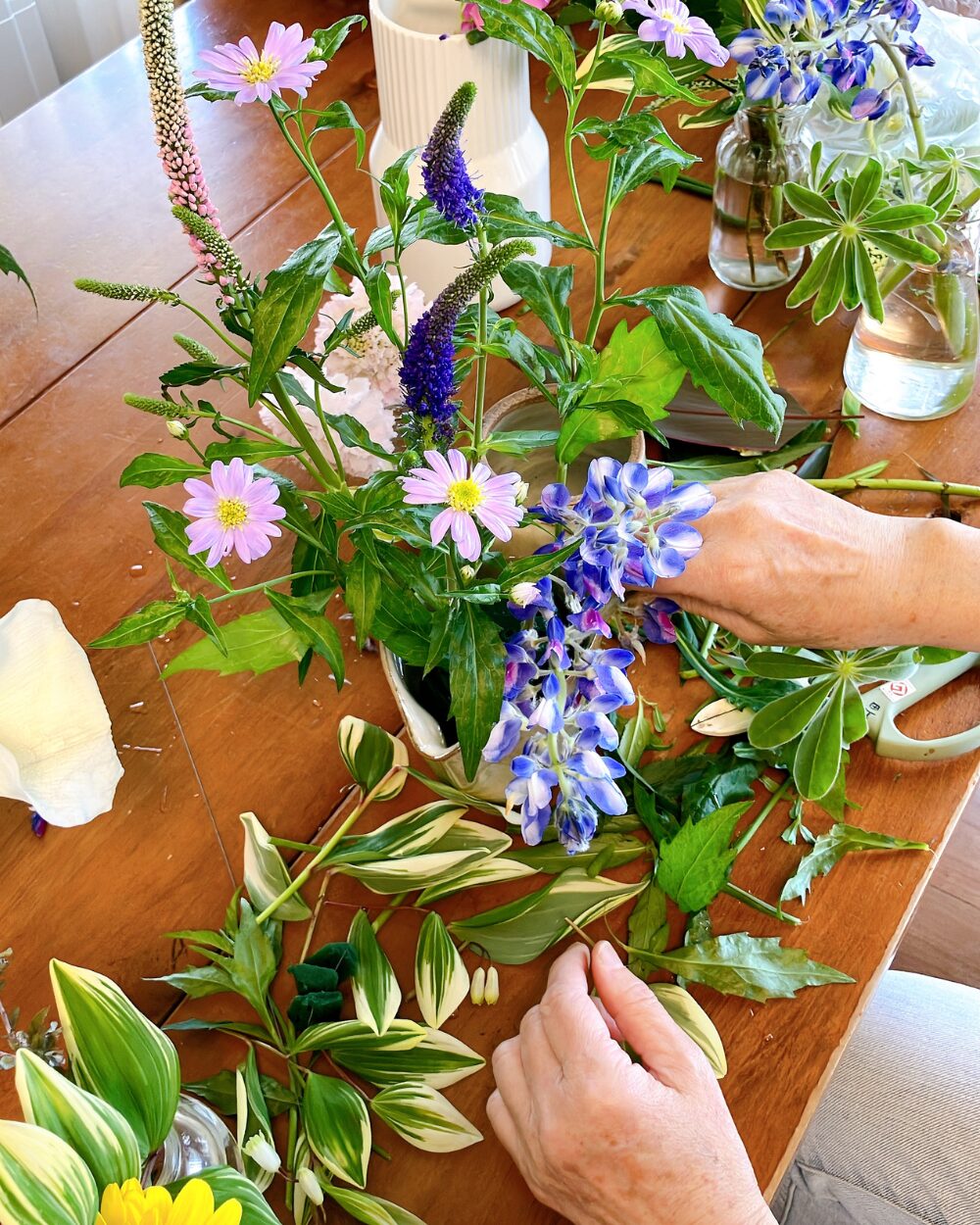 A person's hand arranging blue lupinus and greenery into floral foam for a meadow-style display