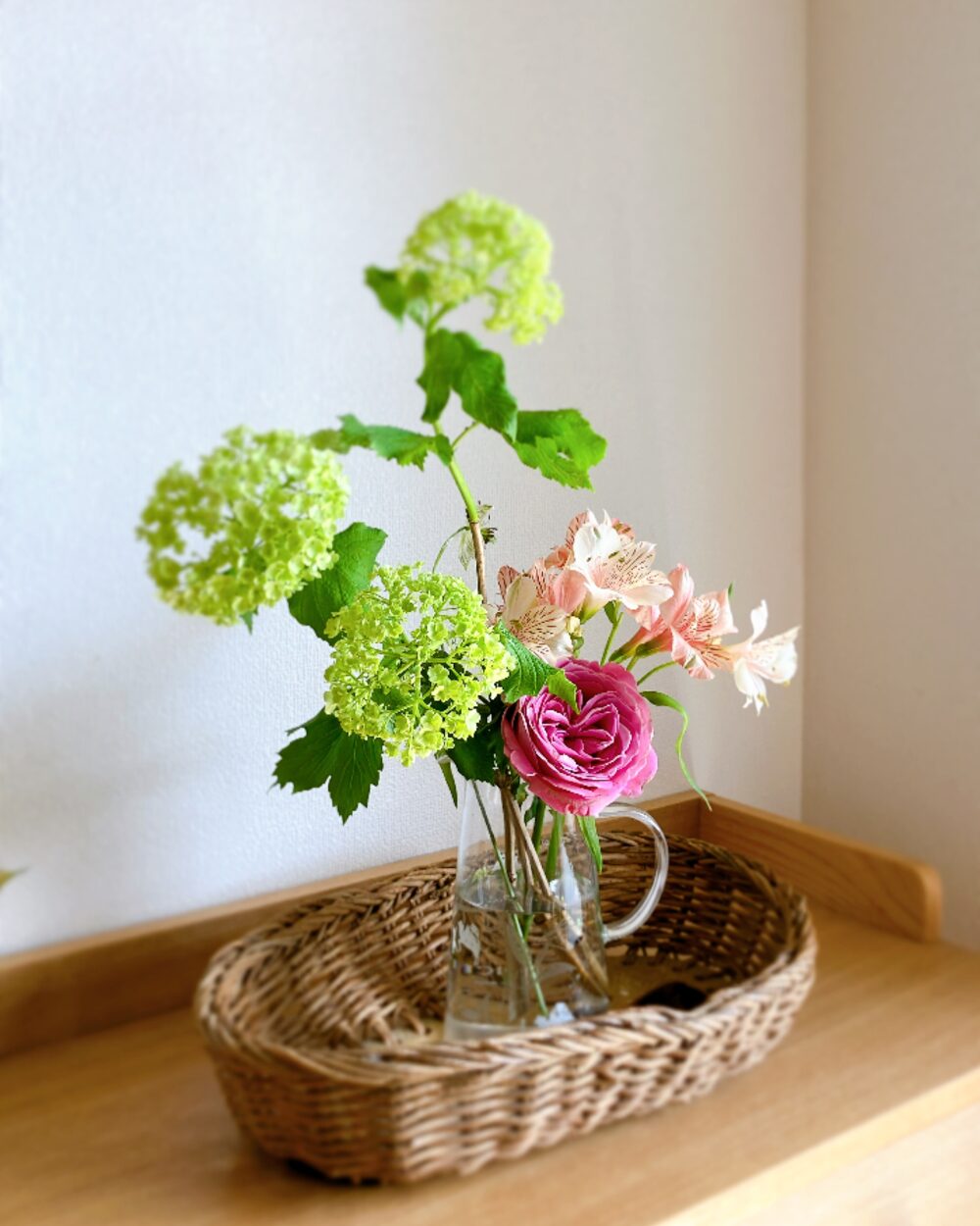 Mixed bouquet of Viburnum Snowball and roses in a glass vase on a woven basket for a natural Japanese aesthetic