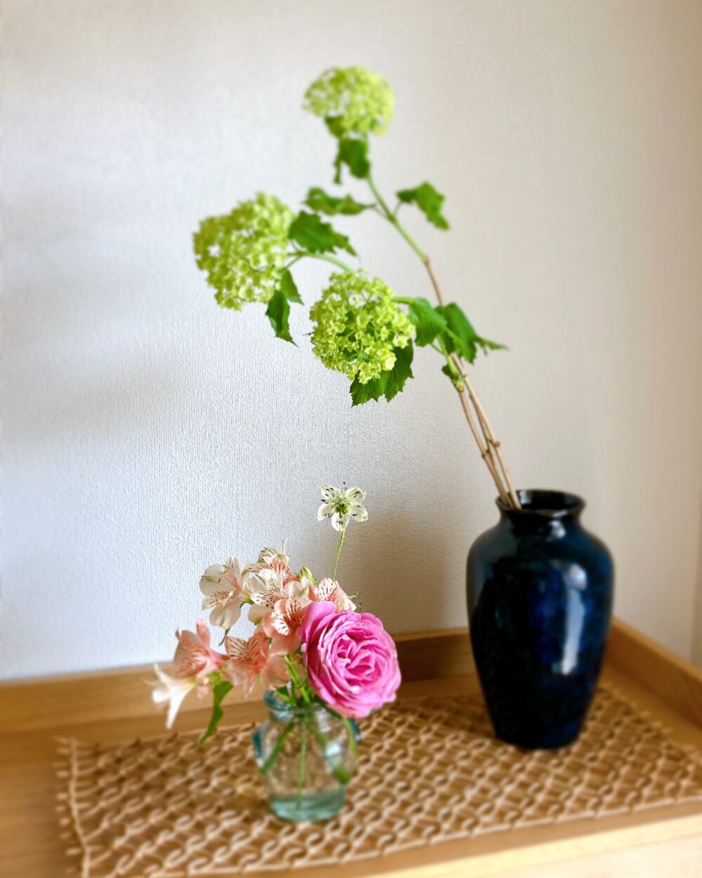 Viburnum Snowball stems in a blue Japanese ceramic vase paired with pink roses in glass, creating a Zen atmosphere