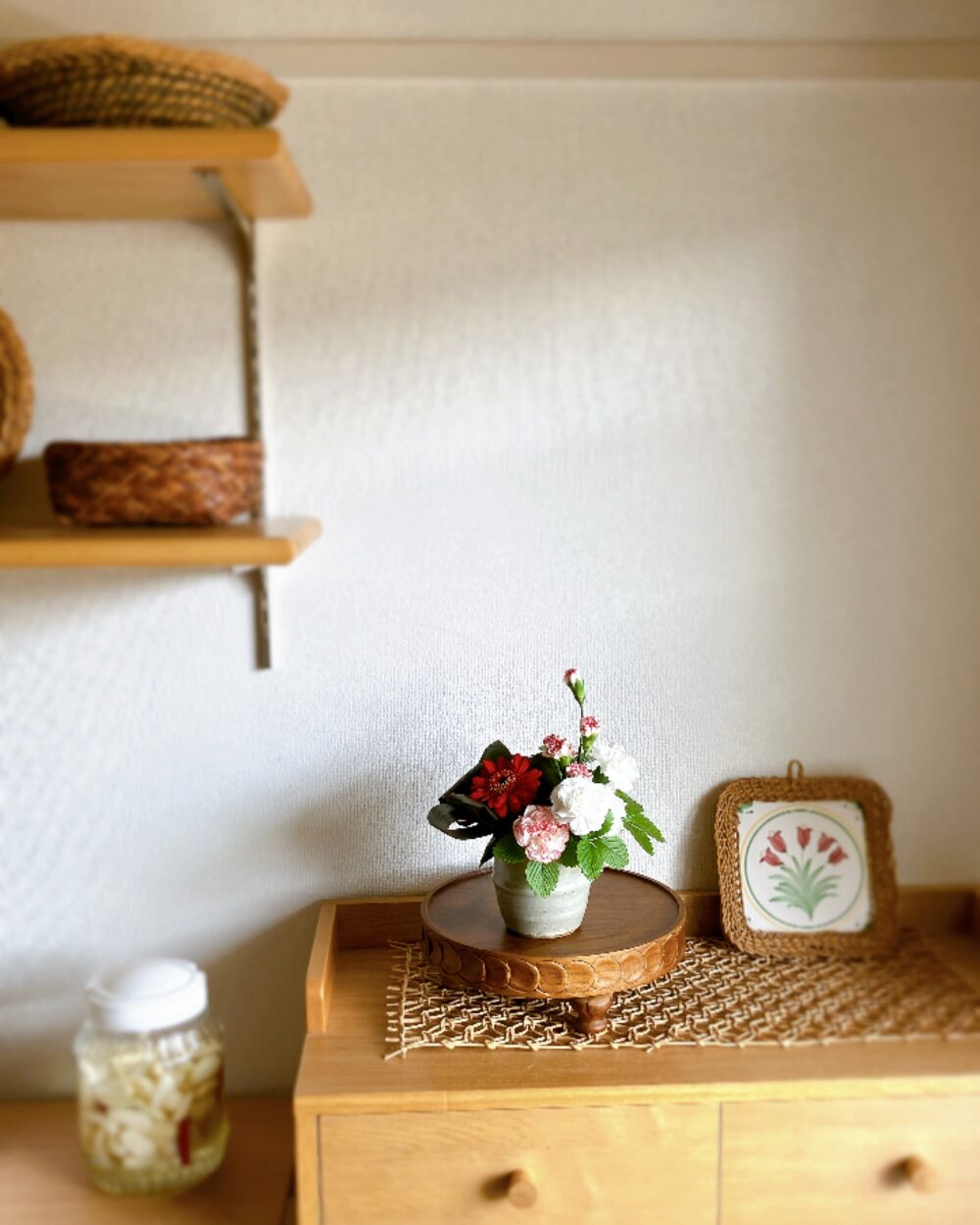 A wide shot of a shelf corner showing a ceramic jar arrangement next to a glass jar of pickled shallots and a basket.
