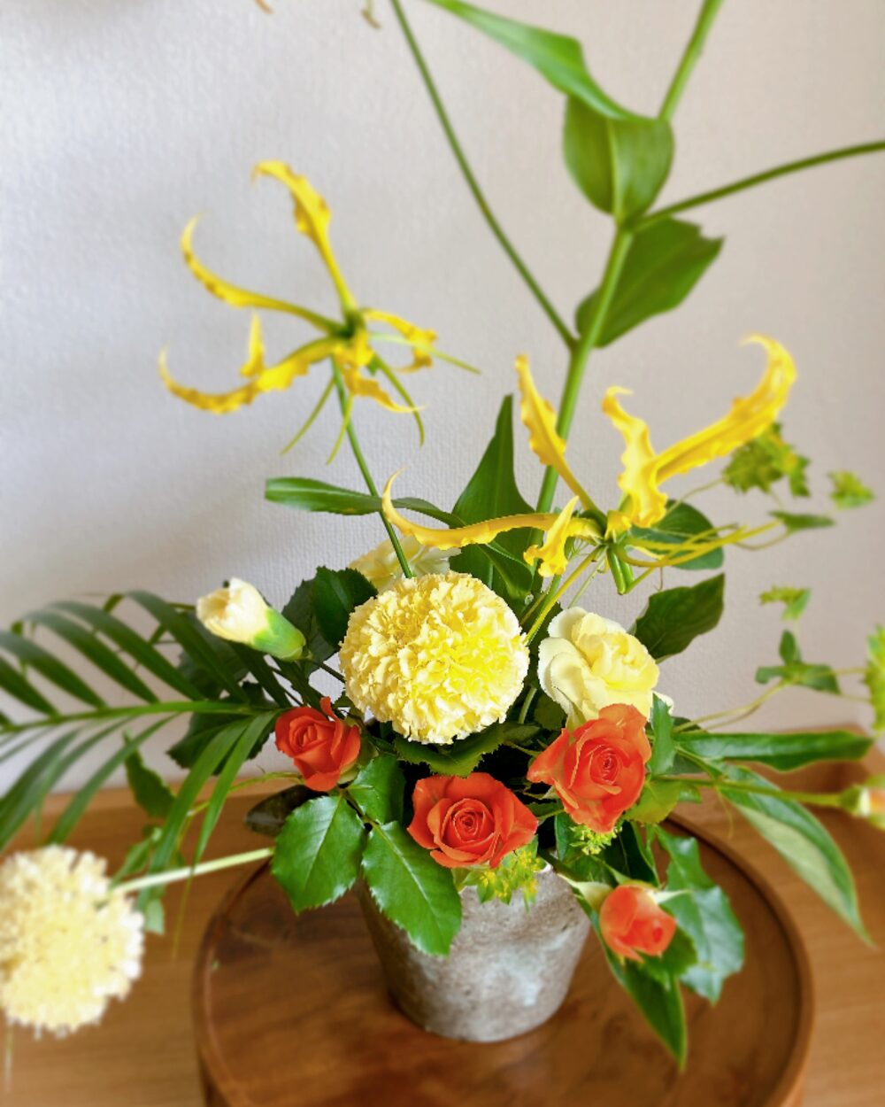 Close-up of yellow marigolds and orange spray roses against the dark, textured surface of a ceramic bowl.