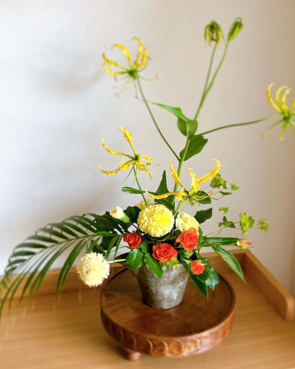 Yellow marigolds, yellow carnations, orange spray roses, and a tall yellow gloriosa in a deep-colored Kasama bowl.