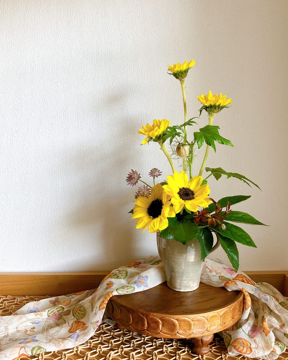 Five sunflowers in a pitcher on a compote with a colorful scarf