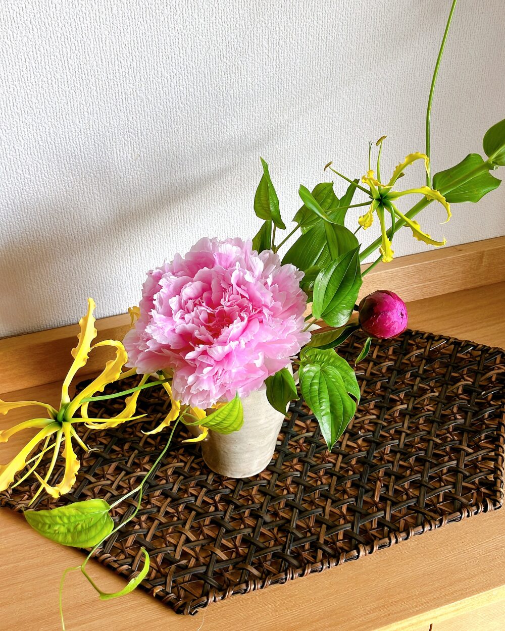 A close-up of a pink peony and yellow gloriosa inside a dark Kasama ceramic server.