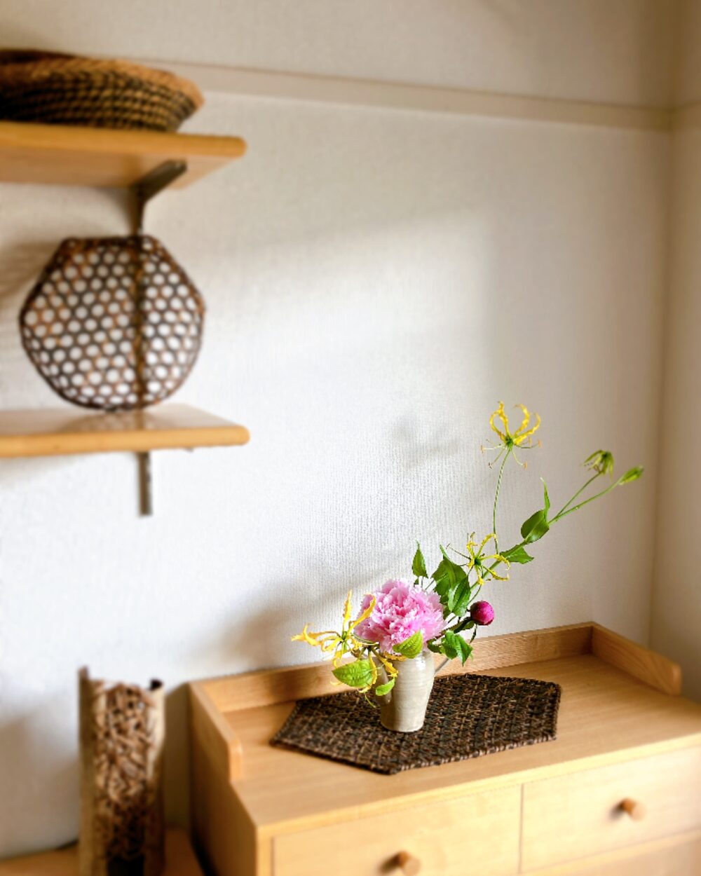A Kasama pitcher arrangement on a dark woven mat next to a bamboo basket on a wooden shelf corner.
