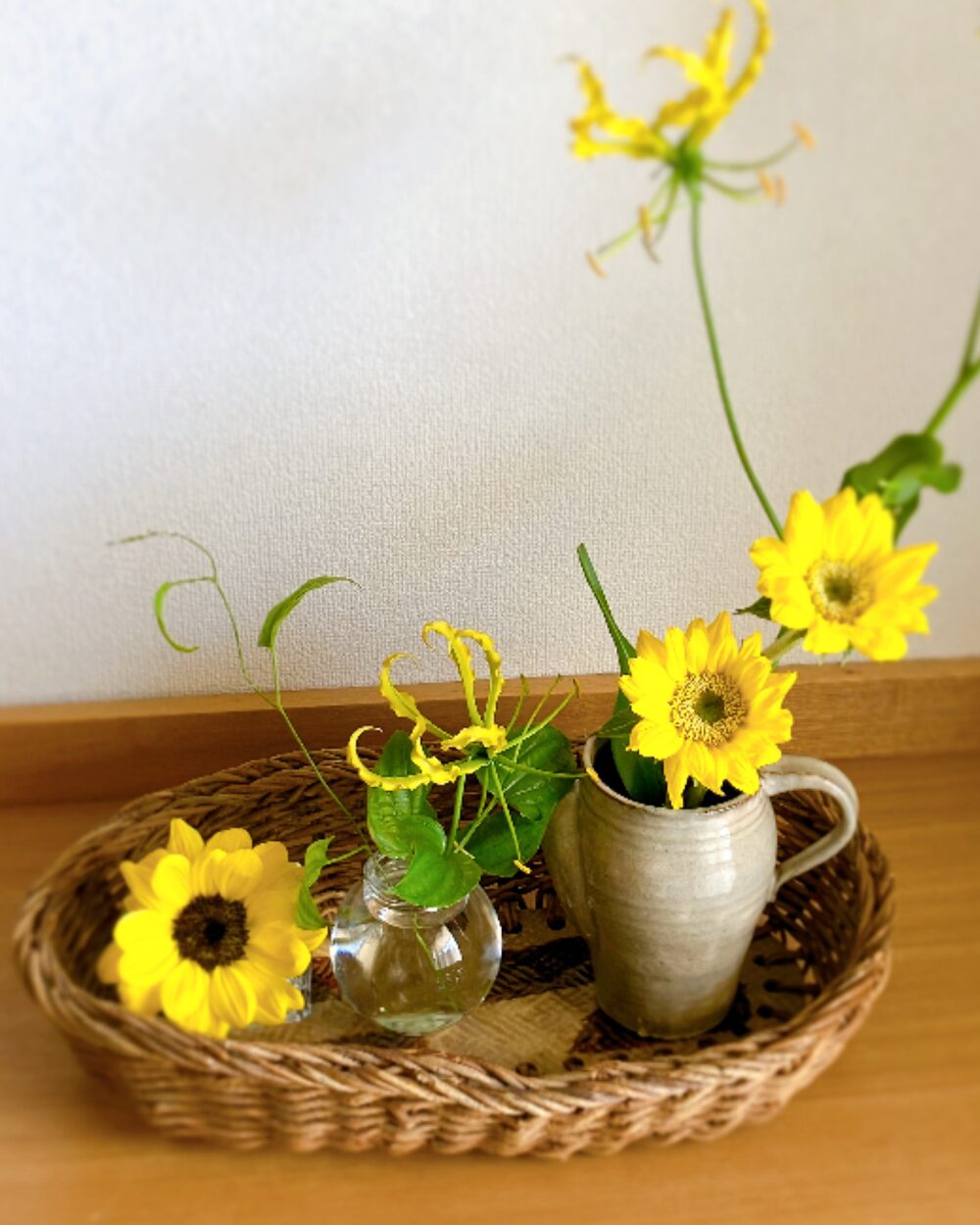 Three small vases with sunflowers and gloriosa inside a tiled basket