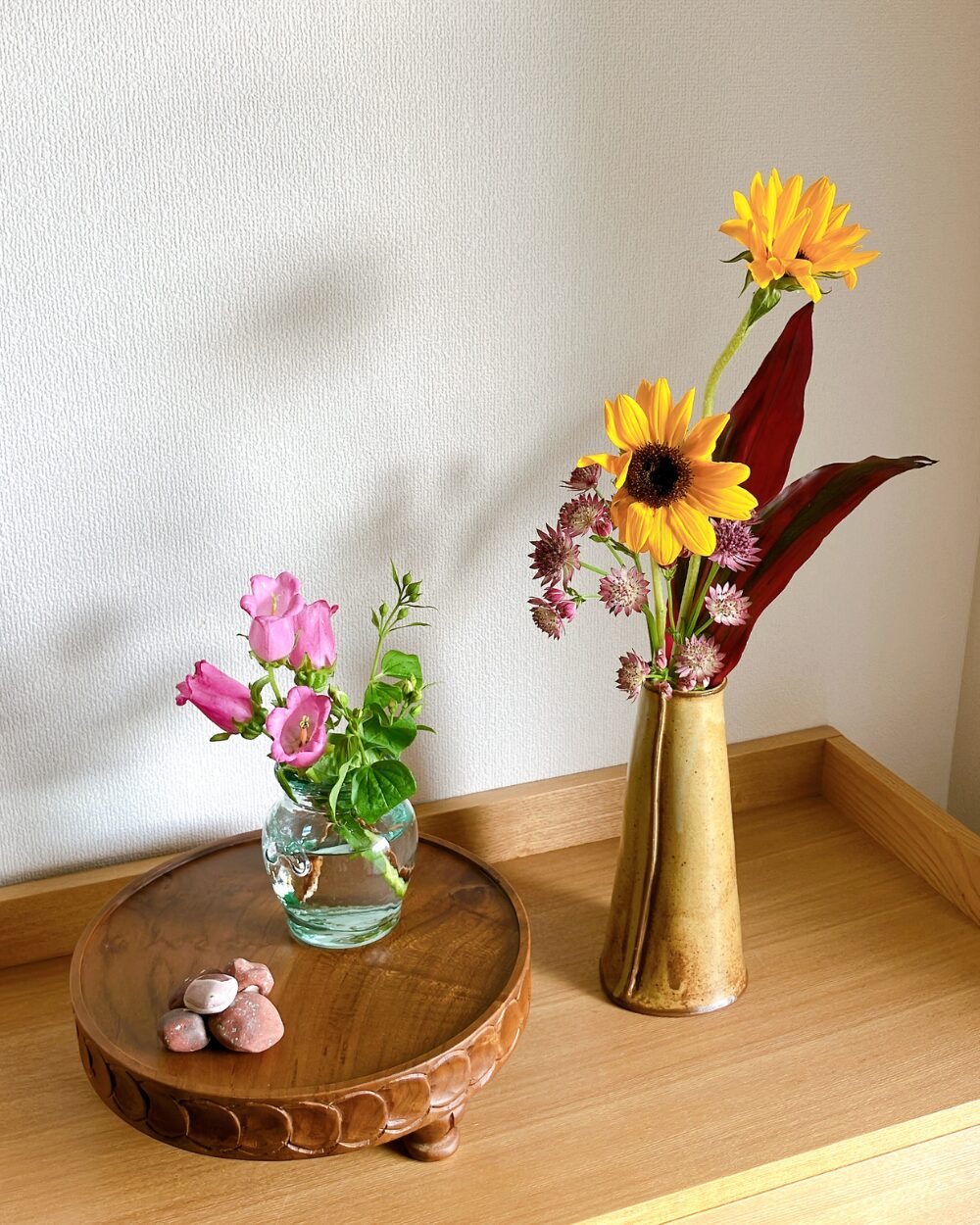 ウッドコンポートの上に置かれたガラス瓶のカンパニュラと、笠間焼の花瓶に生けた初夏のひまわり