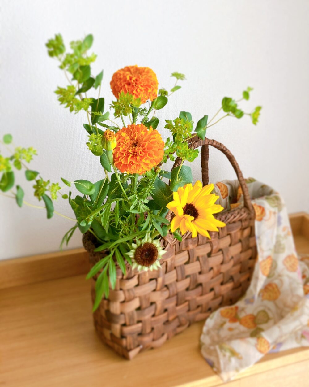 手作りの籠に生けた、花びらを取り除いたひまわりとマリーゴールド、グリーンのモダンなアレンジ