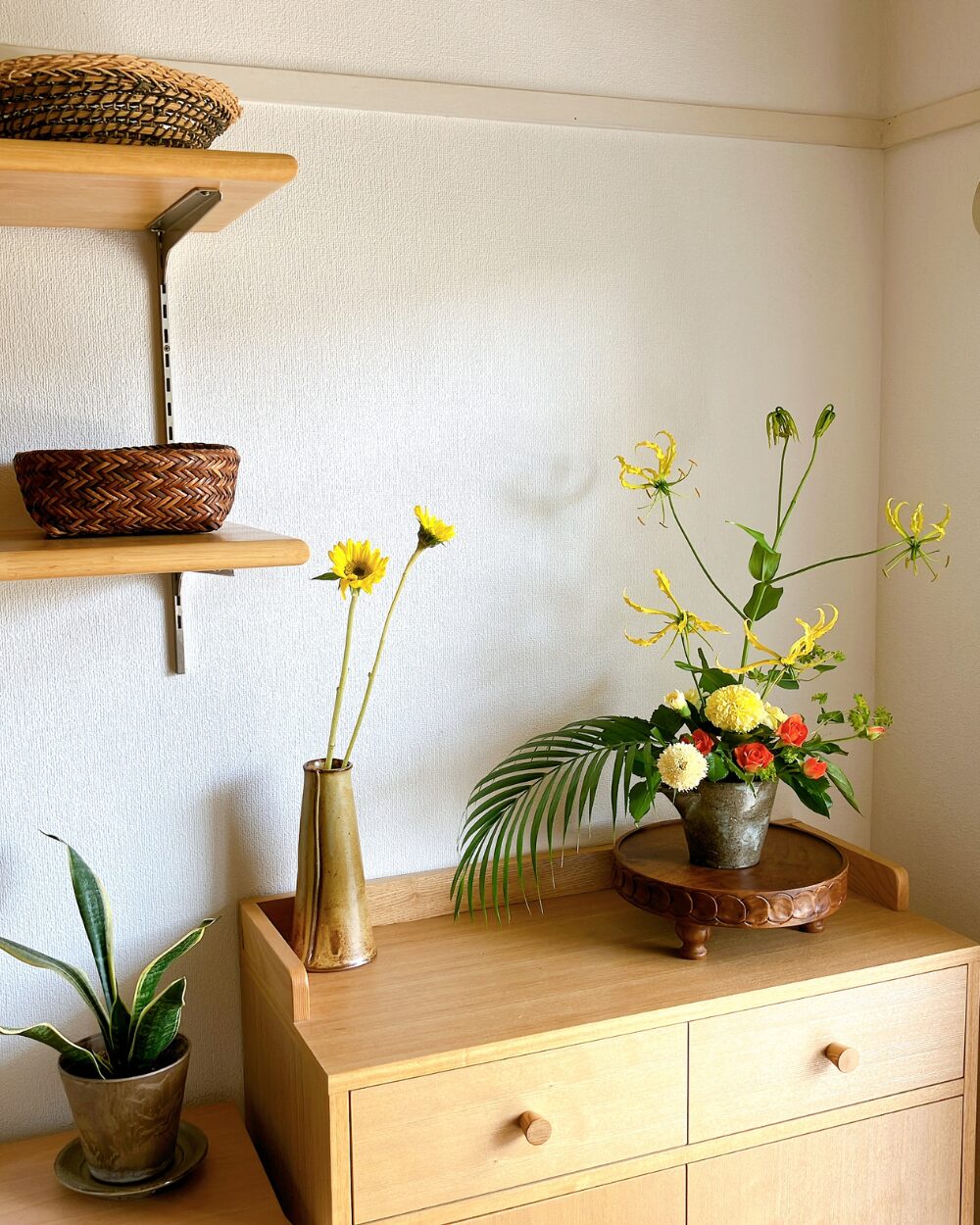 Angled view of a ceramic bowl on a wood compote next to a basket and a small vase with two miniature sunflowers.