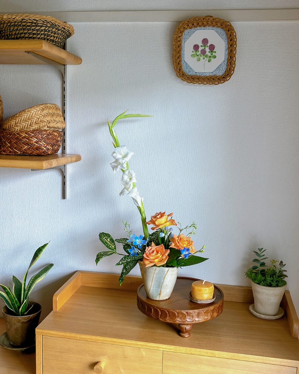 White gladiolus and orange rose arrangement in a ceramic pitcher on a shelf