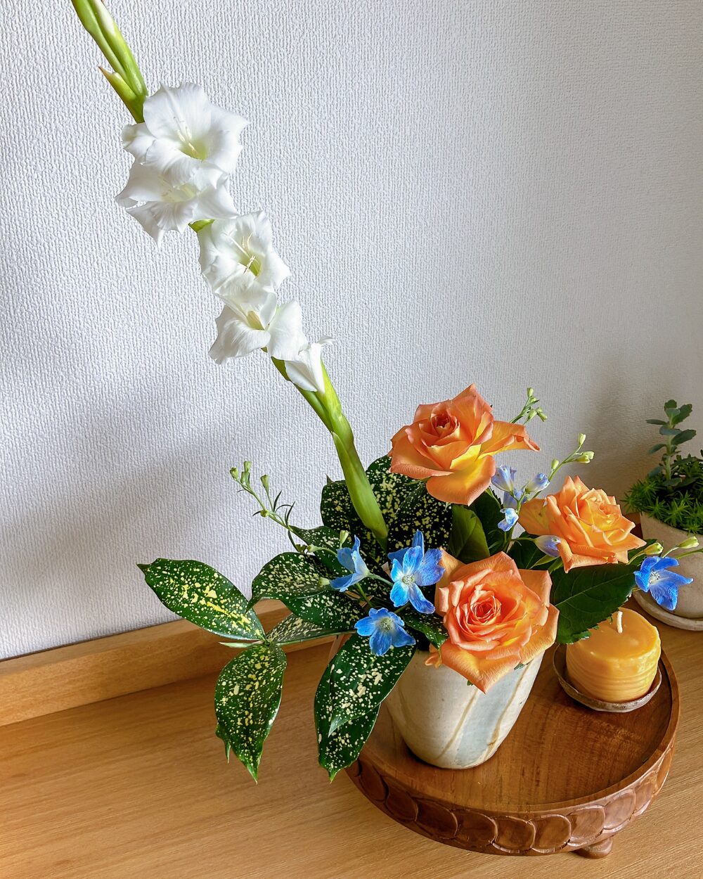 White gladiolus and orange roses in a ceramic pitcher with an orange candle