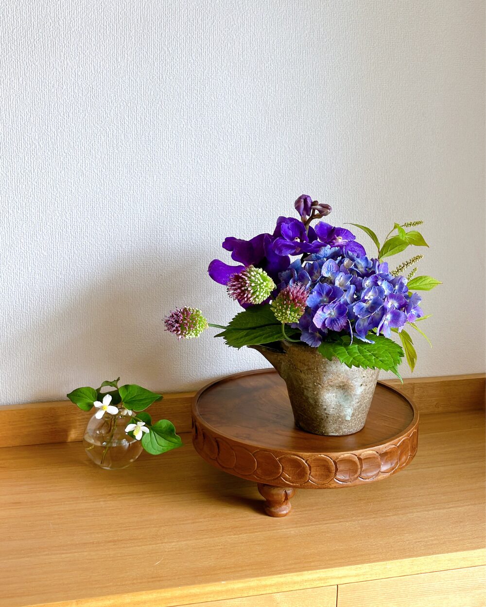 Hydrangea, vanda orchid, and allium arranged inside a dark-colored Japanese ceramic vessel.