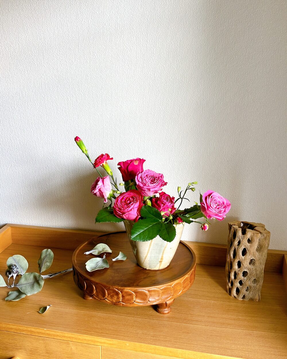 A close-up front view of six pink roses angled in different directions inside a dark Japanese ceramic katakuchi vessel.