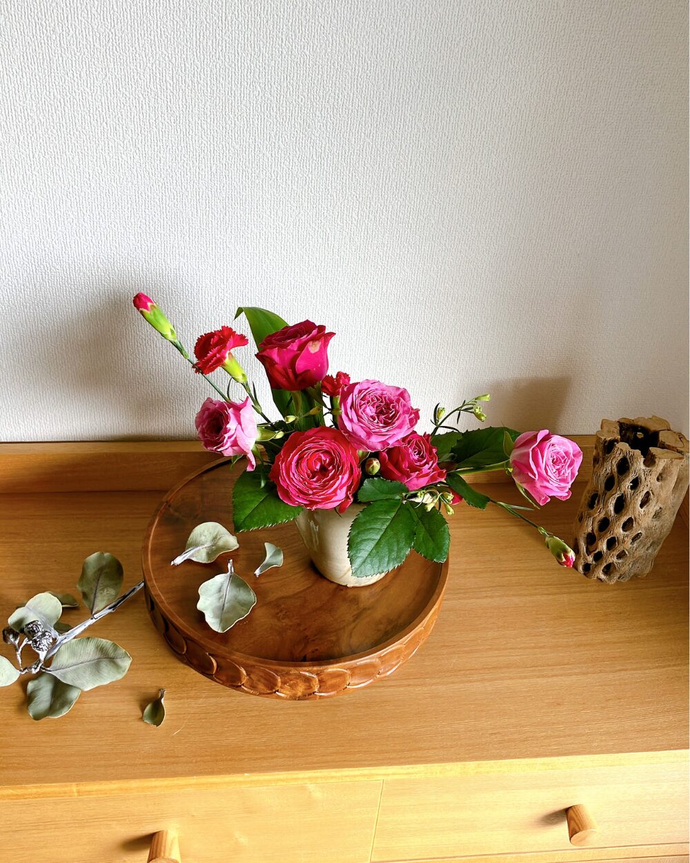 A top-down view of a minimal rose arrangement in a Japanese katakuchi cup, showcasing the varied angles of the pink petals and small buds.