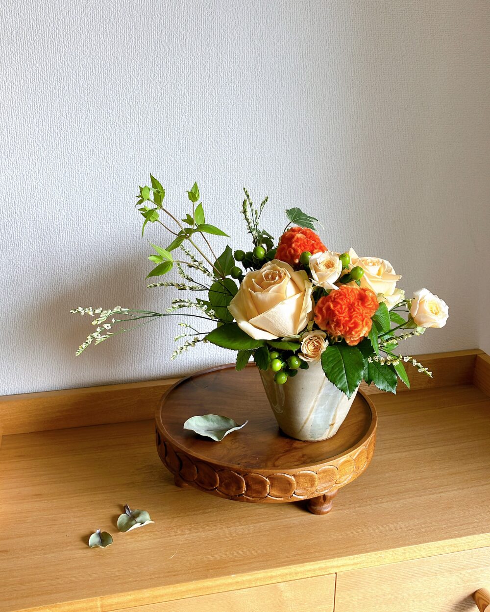 A front view of a plump, rounded arrangement of pale and dark orange roses combined with green hypericum berries in a ceramic vessel.