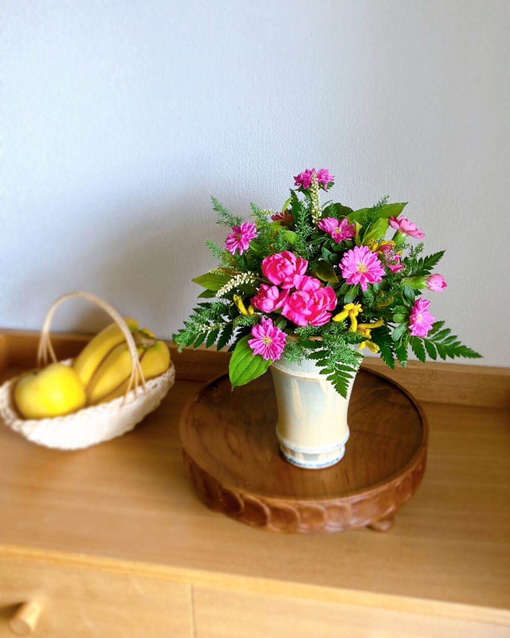 A round flower arrangement with pink asters, pink carnations, and yellow kangaroo paws.