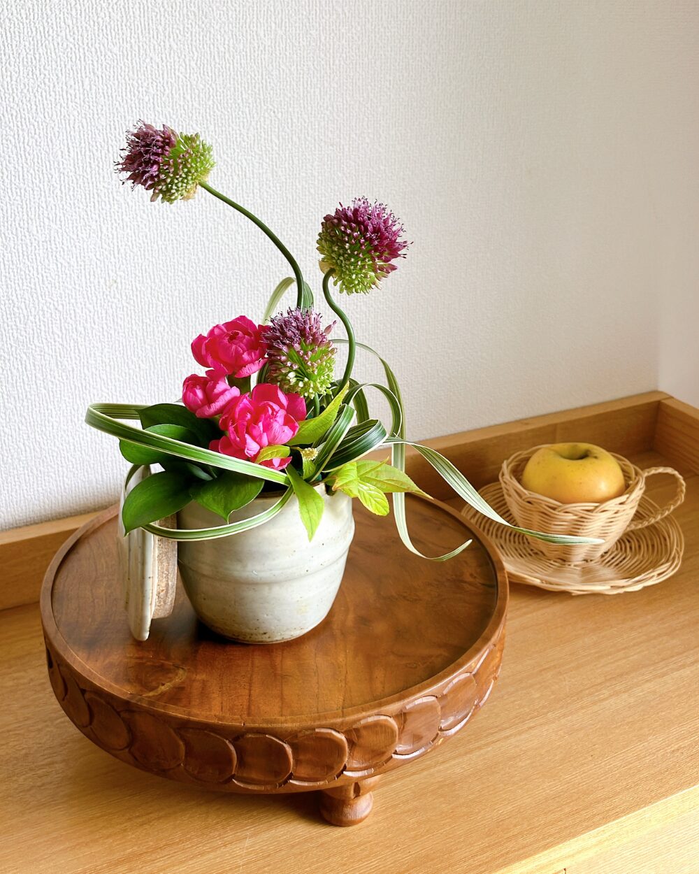Pink carnations and a curved stem of allium arranged inside a small Japanese ceramic jar.